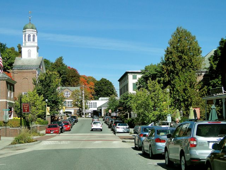 An image of a main street with cars parked along he rode against a blue sky