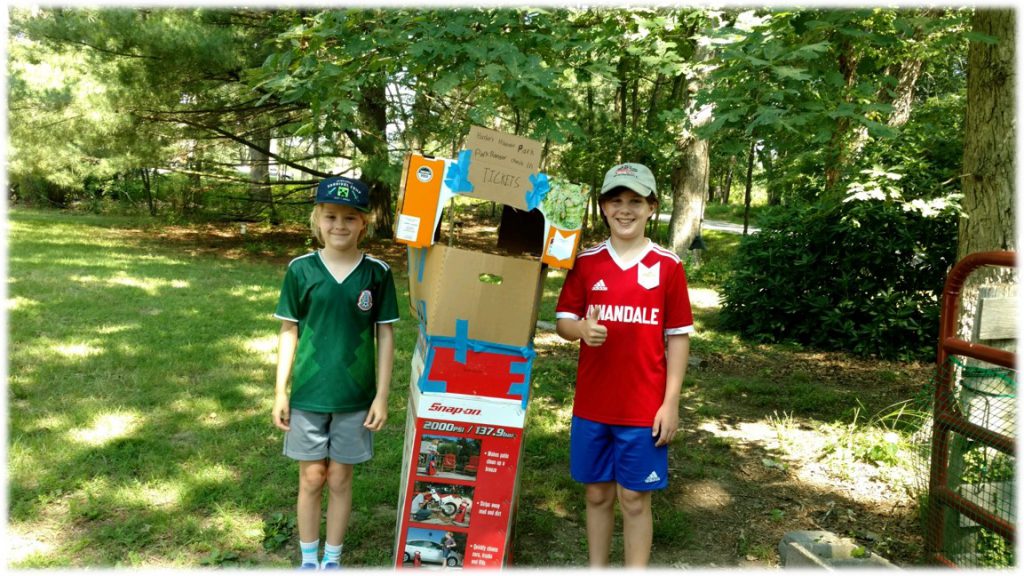 Photo of two kids standing with homemade recycled cardboard ticket booth
