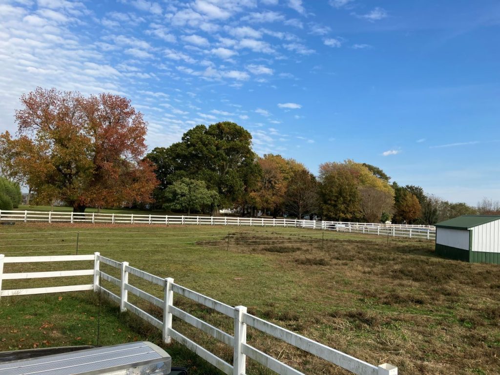 Photo of field surrounded by a picket fence, with trees showing rd, orange, yellow, and green leaves