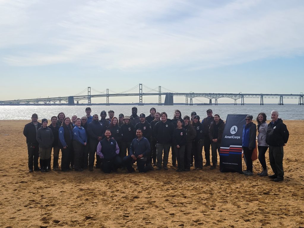 Maryland Conservation Corps members pose with state and AmeriCorps officials in front of the Chesapeake Bay Bridge at Sandy Point State Park. Photo by Joe Zimmermann/DNR