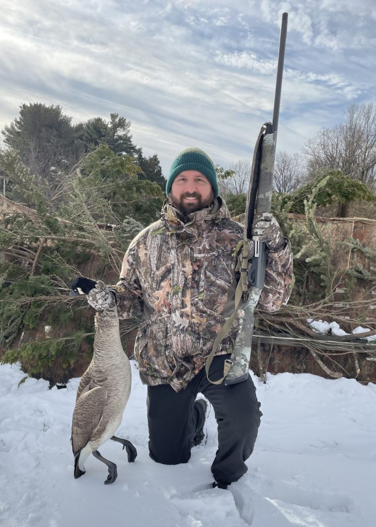 Photo of man holding a shotgun and goose during the winter