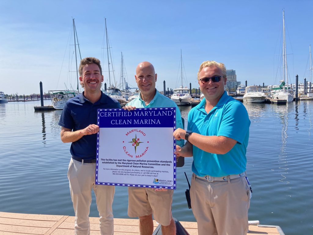 Photo of three men holding a certification sign at a marina