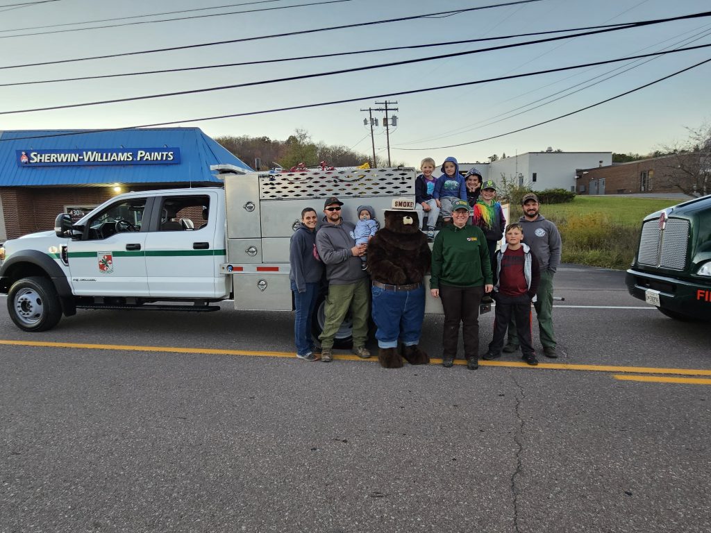 A group of people and Smokey the Bear pose in front of a truck