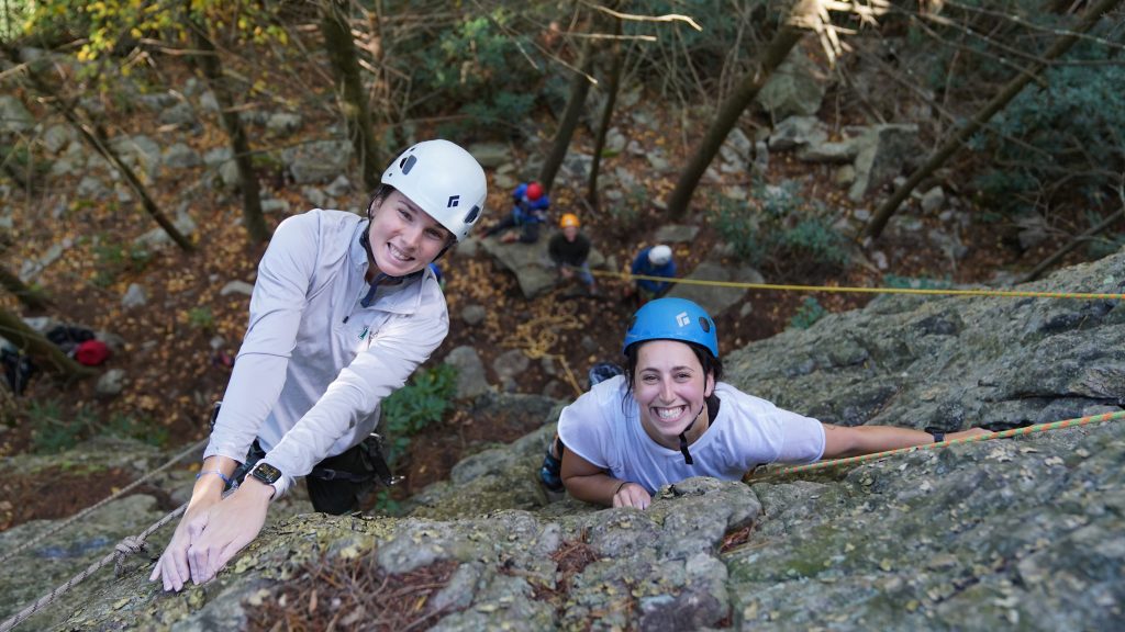 Two people smile at the top of a rock face they have just climbed