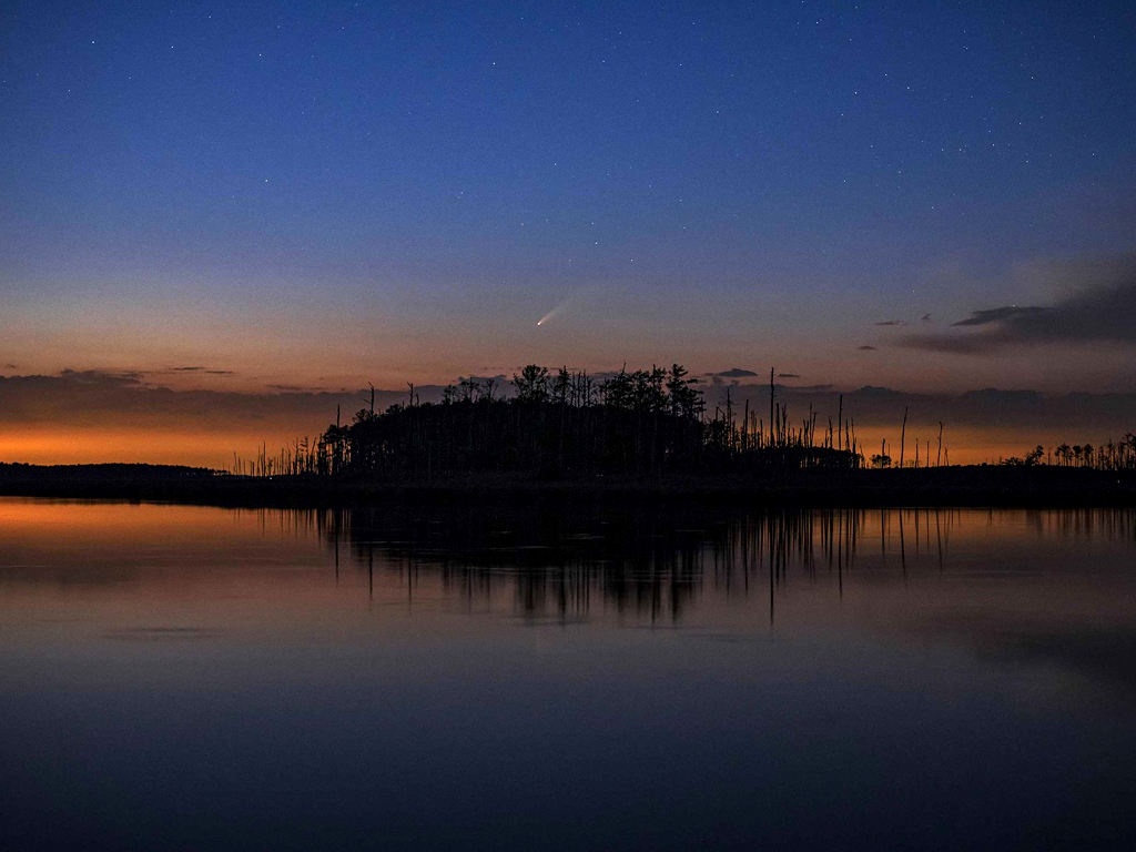 A comet streaks over a small island on the eastern shore.