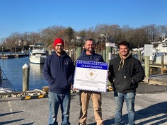 Photo of three men at a marina holding a sign