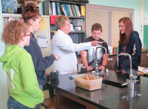 Carol Detrick Garner, 2013 Allegany Co. Teacher of the Year, gathered around table with students performing science experiment. 