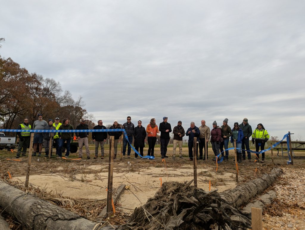 People gathered at a ribbon cutting in front of large logs