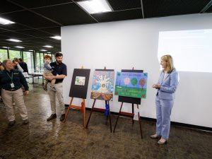 A woman in a forest service shirt stands with a man holding a child and a woman in a blue suit. Between them are winnign entries to the Arbor Day poster contest on easels. 