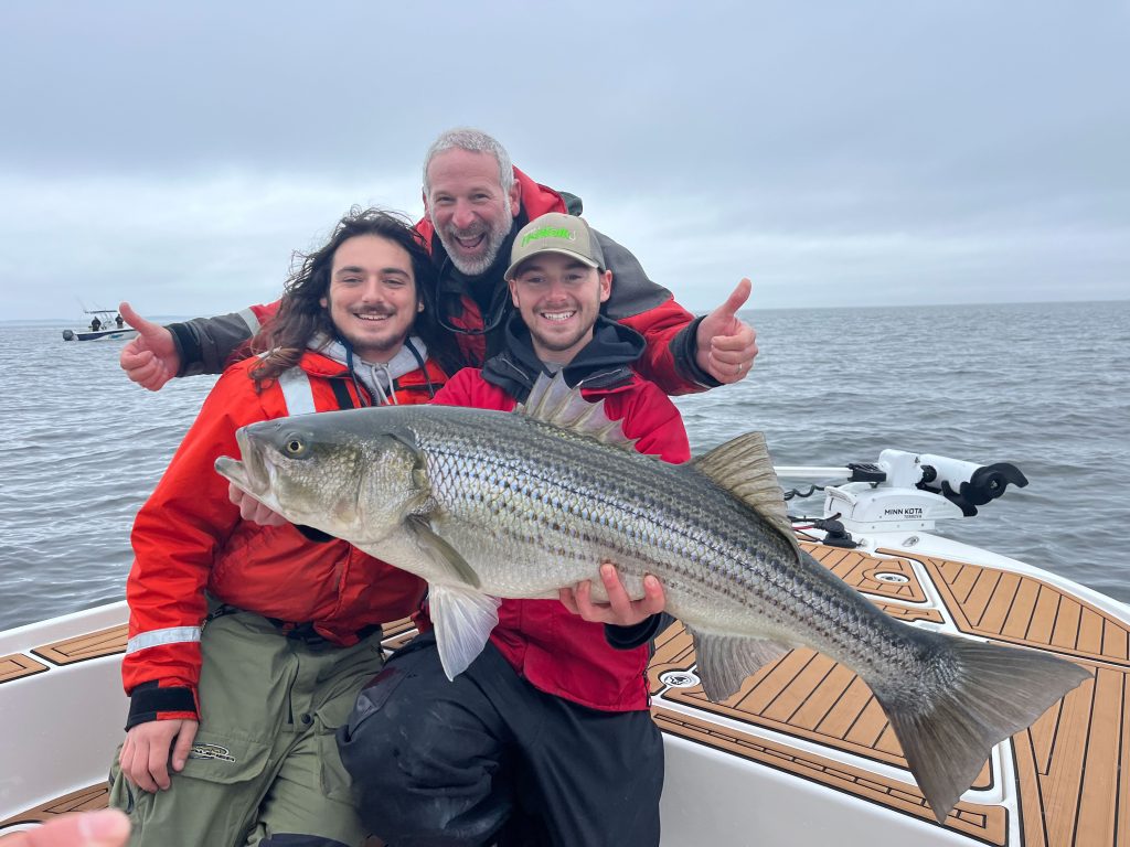 Three men on a boat holding a large fish