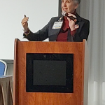 Woman holding a microphone and gesturing with hand while standing behind a lectern